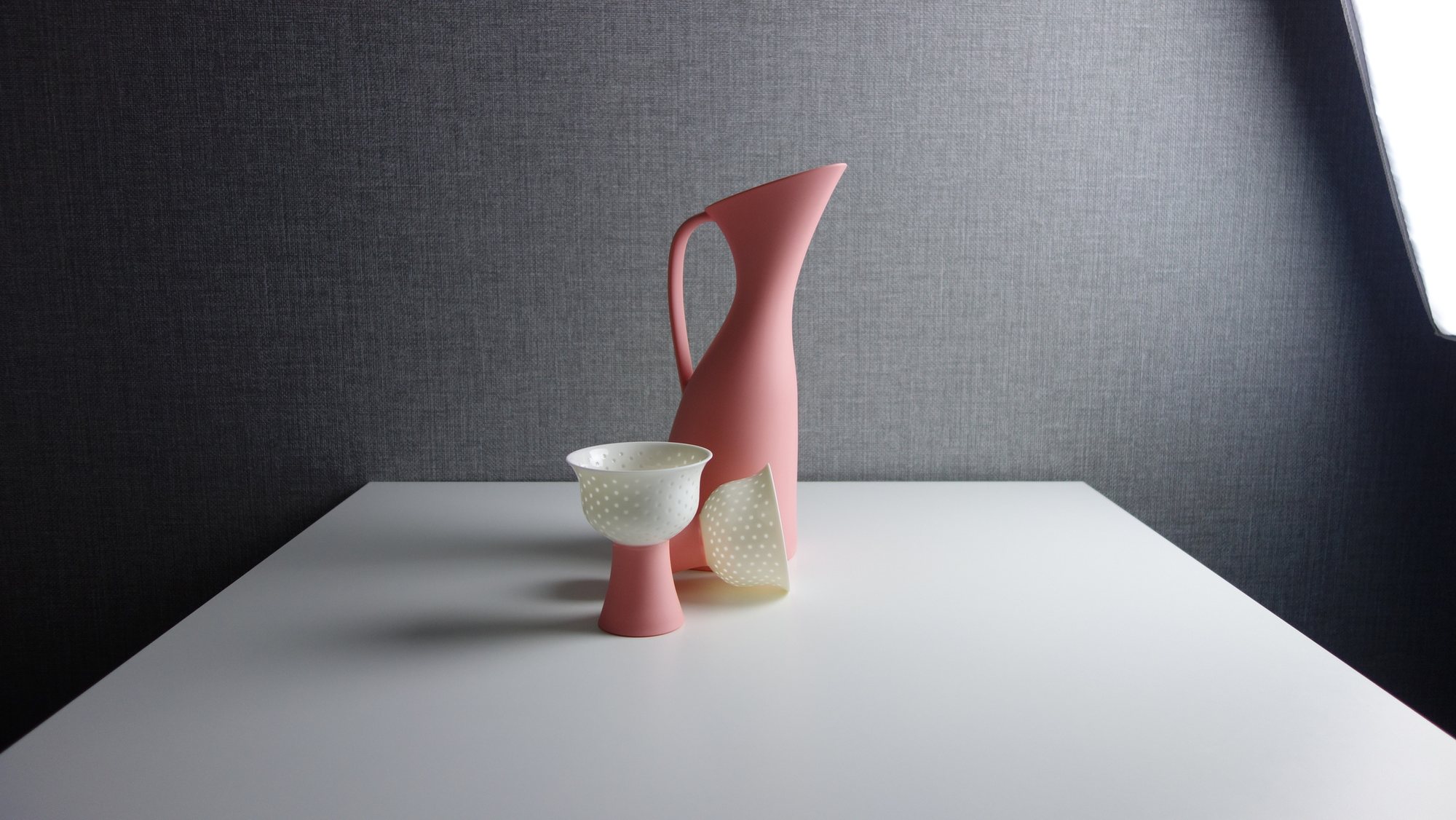 A coral Firefly pitcher behind a pierced white goblet and a tilted cup